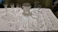 Front view of assorted clear glassware including pitchers, ice bucket, various glasses, and flower vases arranged on white cloth.