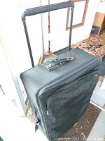 Black Hartmann suitcase standing upright showing telescopic handle extended and top carry handle.