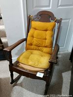 Front view of vintage wooden rocking chair with yellow cushion, visible dark wood frame and missing wicker seat base.