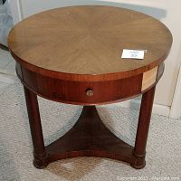 Front view of the brown round laminate end table showing the drawer, legs, and triangular base support.