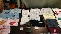 Photo showing assortment of tee shirts organized by size from child to adult XL, with a Mason baseball cap in front center.