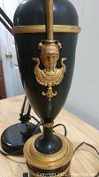 Close-up of black and brass ornate lamp body showing decorative figure and detailed banding.