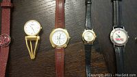 Five vintage wristwatches laid on table with varying strap colors and brand markings visible