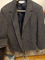 Close-up of the Dress Barn plaid dress jacket hanging on a wooden hanger, showing the collar, fabric pattern, and inner lining.