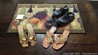 Photo showing three pairs of women's shoes on a colorful wine-style door mat