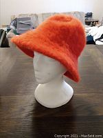 Orange fuzzy bucket hat displayed on a white mannequin head, showing soft fuzzy texture and bucket style