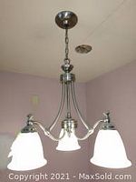 Full view of chandelier hanging from ceiling with three frosted glass bell-shaped shades and brushed nickel finish