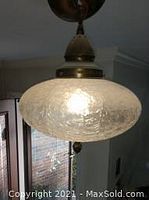 Clear textured glass globe pendant light hanging from ceiling showcasing lit bulb and metal fixture.