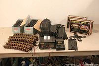 Full view of lot showing Lionel brass and black plastic tracks, Aristo-Craft transformer, accessory track boxes, and other plastic track pieces on display table.