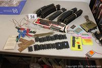 Wide view of the LOT showing bundled black plastic HO scale curved and straight track pieces, switch controllers, small accessories, and transformer on a table.