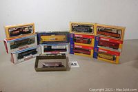 All 12 boxed HO scale rolling stock arranged showing packaging and brands. Variety of models: tanker, gondolas, hopper cars, caboose, freight cars.