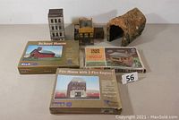 Full lot overview with two built buildings, three sealed model kits, one open kit box, and a vintage modeled tunnel.