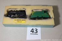 Both locomotives resting in a foam insert inside a box labeled 'YARD HOG SWITCHER'. The black Pennsylvania engine on the left, green Marx engine on the right.