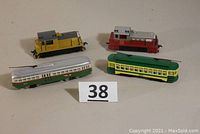 Four HO scale model train engines on flat surface with lot number card including green/cream PTC trolley, green/yellow trolley, yellow Santa Fe #241 switcher, red/gray Union Pacific #720 switcher