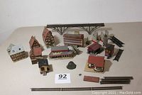 Photo showing overall 10 built-up N Scale structures including buildings and a metal arch bridge, arranged on a plain surface with model railroad track sections.