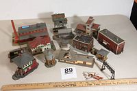 Overview photo showing all 11+ built-up N scale structures of varied types including factory and railroad-related buildings with a ruler for scale.