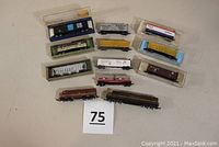 Overview of all locomotives and freight cars arrangement, showing 2 locomotives and 10 freight cars in various colors and designs with some in plastic cases.