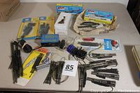 Full lot view showing various N scale turnout switches including boxed Atlas snap switches, loose switches, wiring, and controllers on table.