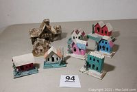 Nine vintage Putz cardboard Christmas houses in varied colors arranged together on a plain surface.