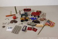 Overview of assorted vintage toys including Marx wind-up race car, toy tractor, metal wagon, plastic cars, license tags, small flag, and various toy parts.
