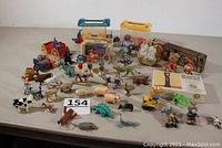 Wide view of multiple plastic farm animals, various plastic animal and human figurines, small toys including a wagon and tractor, and a boxed dollhouse kit.