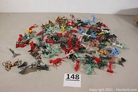 Wide view showing a large collection of multicolored plastic toy soldiers and Native Americans arranged loosely on a table, including some siege weapon accessories.