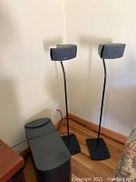 Full view of two Bose speakers mounted on stands next to a Bose subwoofer on the floor.