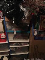 Four stacked plastic totes stored in a basement area, containing Christmas ornaments visible inside the translucent containers.