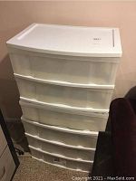 Photo of one white plastic storage organizer with three drawers, stacked on another similar unit, against a wall with beige paint.