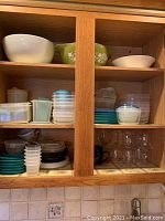 Cabinet shelves containing Pyrex mixing bowls and multiple plastic containers with lids in various sizes and colors.