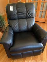 Full front view of the black leather recliner rocker chair showing the padded bulky seat and backrest.