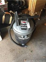 Gray and black Shop-Vac wet/dry vacuum with hose and nozzle attachment, positioned upright on concrete floor.