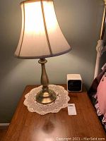 One Stiffel brass lamp lit on wooden nightstand with lace doily and Sony Dream Machine clock radio