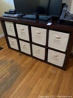Full front view of the wooden cube storage cabinet with eight white fabric pull-out bins arranged in two rows and four columns.