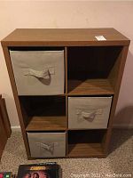 Front view of the cube storage cabinet showing three beige fabric bins and three empty compartments.
