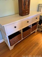 Full view of white wooden table showing three drawers and three wicker bins below.