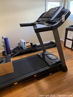 Side view of the NordicTrack treadmill inside a room on a wooden floor, showing box and items on the treadmill belt.