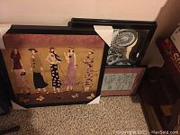 Four framed wall art pieces stacked and leaning against wall, showcasing variety in styles and sizes.