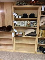 Photo showing two wooden shelving units side by side, light wood with multiple shelves. The taller unit has more shelf space than the shorter one.