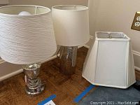 Two mercury glass base lamps with white shades and one extra white lamp shade on floor, showing overall lot contents and sizes.