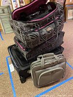 Stack of luggage and totes showing zebra print Anne Klein duffle and suitcase, black Delsey suitcase, and taupe tote.