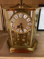 Front view of Seth Thomas German clock showing gold dial with Roman numerals inside brass and glass hexagonal case.