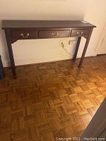 Full view of the dark wood console table showing its overall shape, drawer placement, and brass handles.