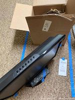 Side view of LG television with remote control placed on base, black color TV with buttons on side.