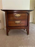 Front view of the Asian style night stand showing two drawers with ornate metal pulls and wooden body.