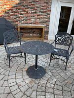 Full view of round black wrought iron table with two matching chairs outside on stone patio.