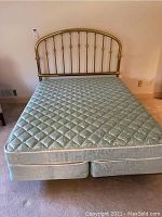Overall view of queen mattress and box spring on brass headboard bed frame, shows full setup of bed