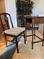 Solid wood chair with cushioned seat and intricate chair back, positioned next to the phone table