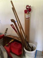 Photo showing three shovels, two red plastic gas cans in large wicker style basket, and some driveway reflectors.