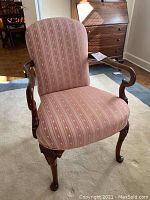 Front view of one upholstered accent chair showing mauve floral brocade fabric and carved wood curved arms and legs.